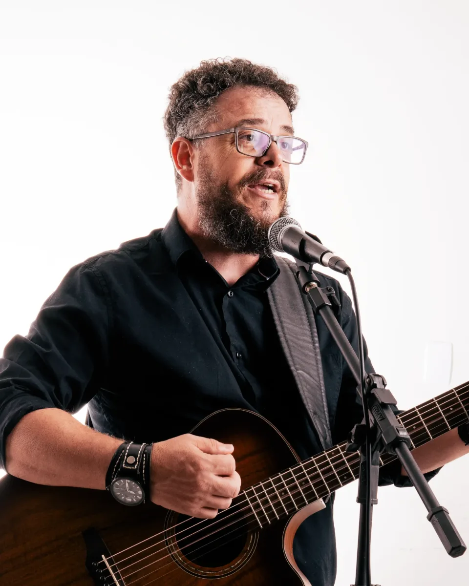 Carlinhos Falsetti cantando ao microfone com o violão