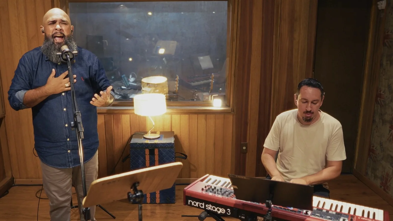 Vitor Teixeira canta ao microfone enquanto um músico o acompanha ao teclado, no estúdio, durante a gravação do videoclipe de «Deus, Oh Deus»